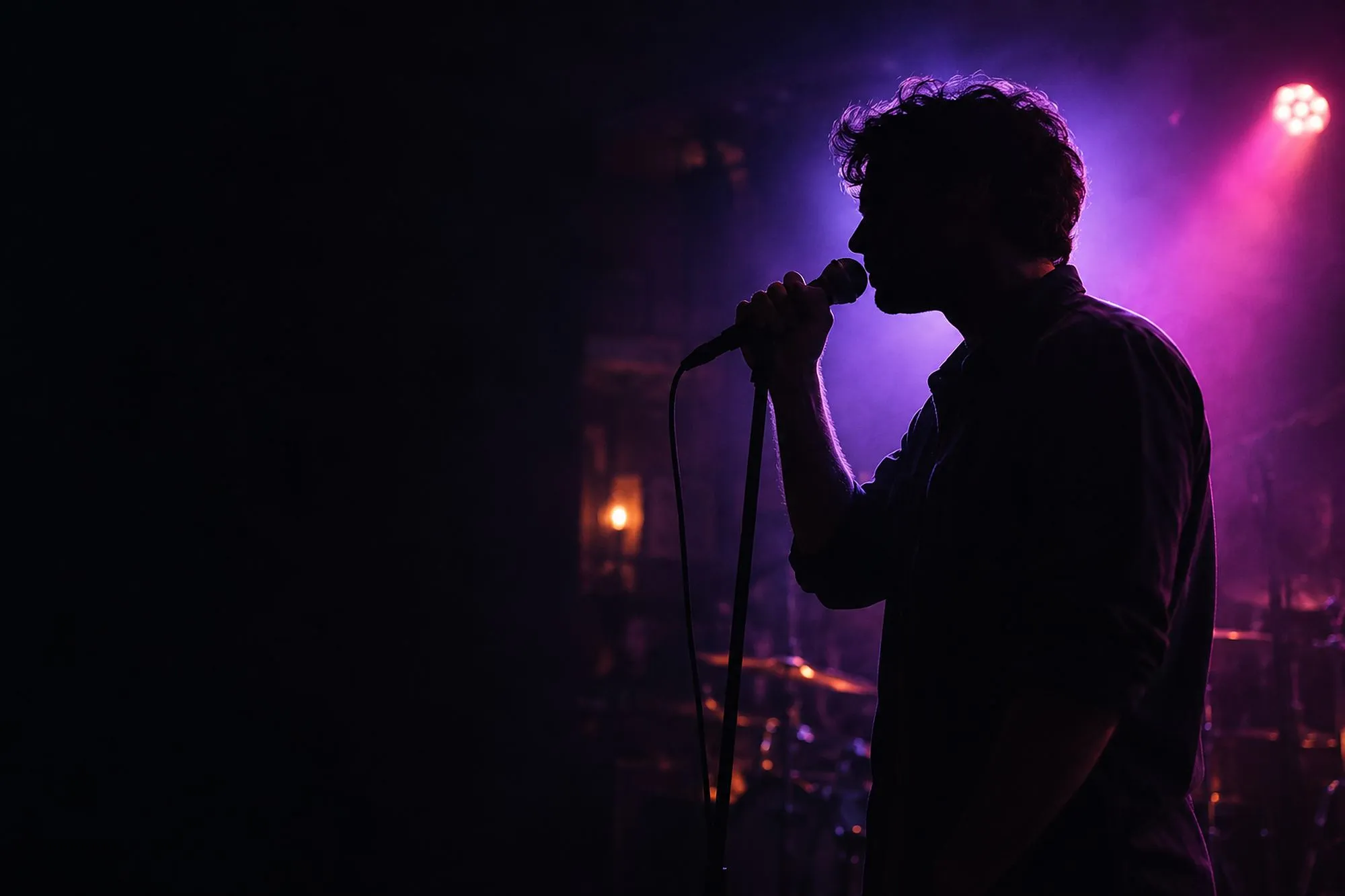 A singer in silhouette at a microphone on a small bar stage, violet spotlight and drums behind