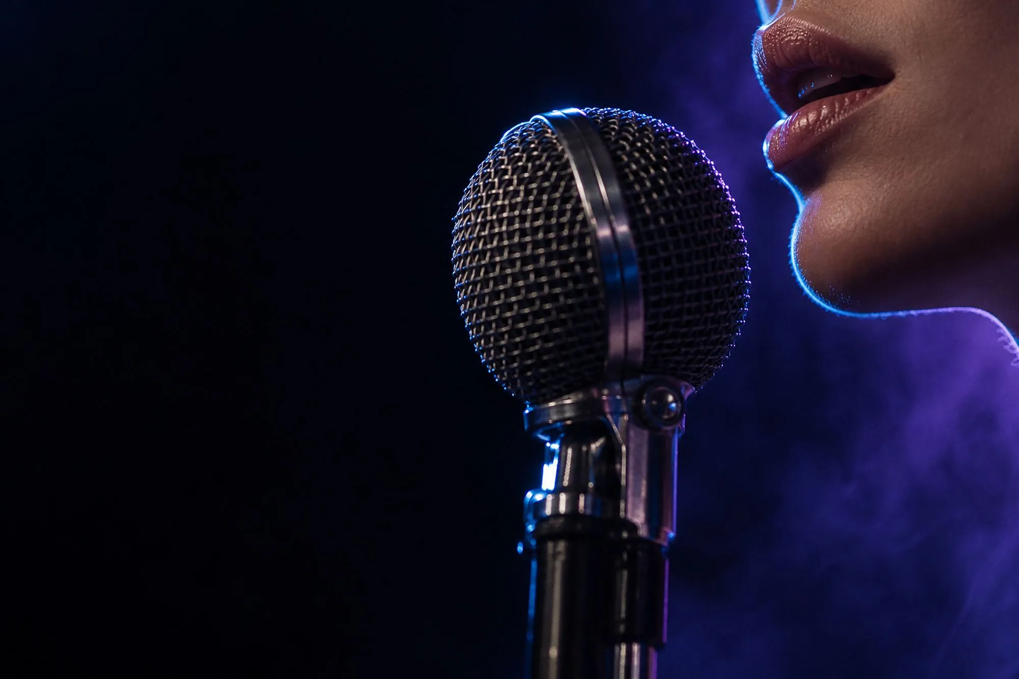Close-up of a singer’s lips and chin at a chrome microphone in blue rim light