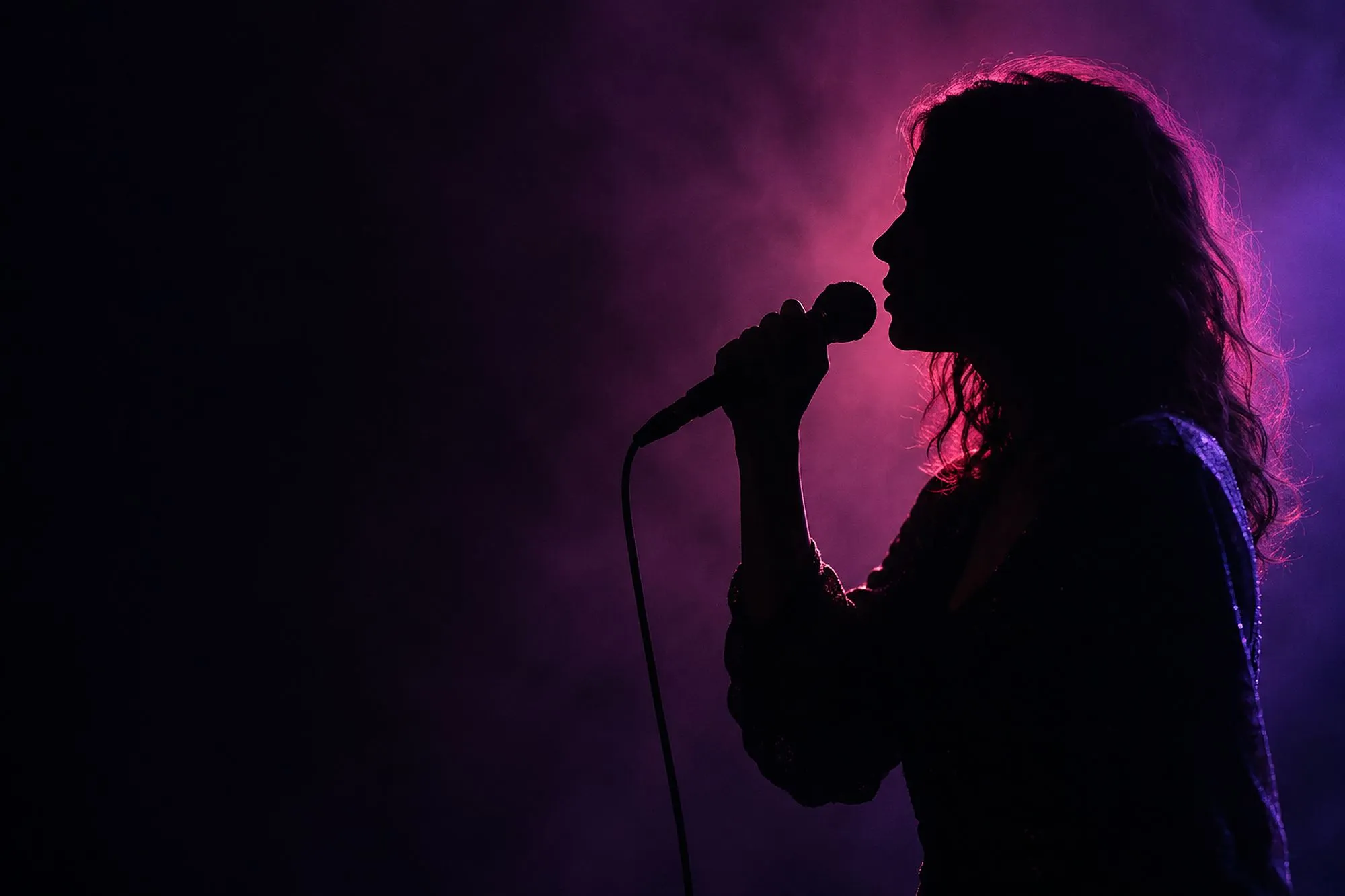 A singer in profile silhouette sings into a handheld microphone, backlit pink and violet through haze